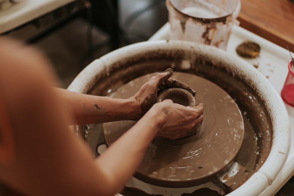 Hands centring wet clay on a pottery wheel during a beginner class