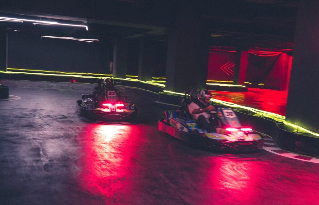 Two drivers racing electric go-karts on a red neon indoor track in Gurugram